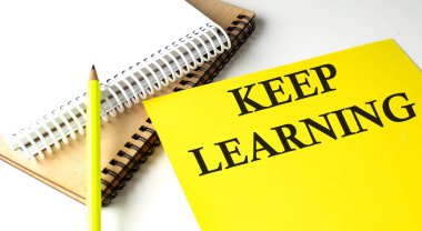 KEEP LEARNING text written on yellow paper with notebook clipart