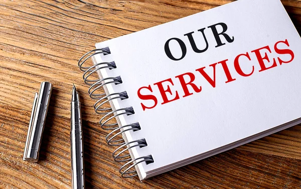 OUR SERVICES text on a notebook with pen on wooden background