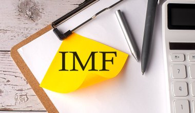 Hesap makinesi, kalem ve panosu olan sarı yapışkan bir IMF kelimesi