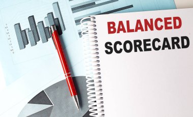 Not defterindeki balanslı SCORECARD metni ve arkaplanda bir kalem