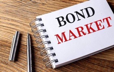 Tahta zemin üzerinde kalem olan bir defter üzerindeki BOND MARKET metni