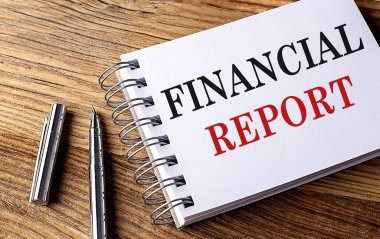 Ahşap zemin üzerinde kalem olan bir not defterindeki FINANSIAL REPORT metni