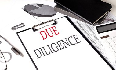 Arkaplanda çizelge ve defter bulunan bir kağıt pano üzerindeki DUE DILIGENCE metni
