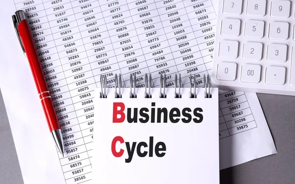 BUSINESS CYCLE text on notebook with pen, calculator and chart on a grey background
