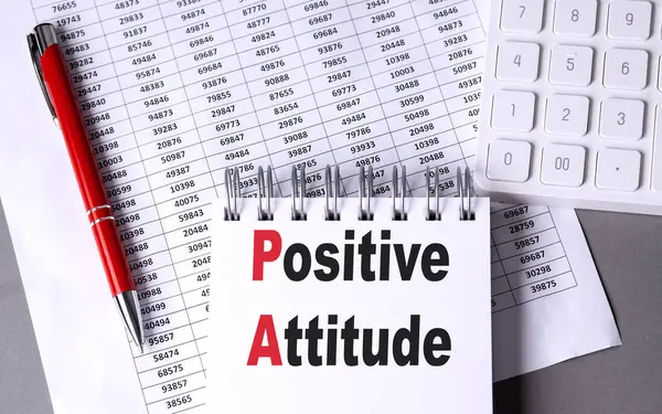 POSITIVE ATTITUDE text on a notebook with pen, calculator and chart on grey background