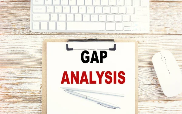 GAP ANALYSIS text on paper clipboard with keyboard on wooden background