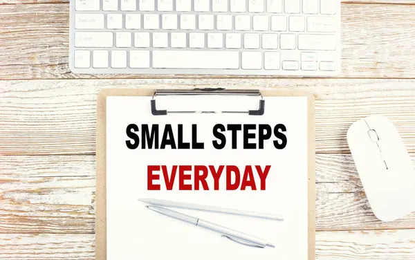 SMALL STEPS EVERYDAY text on clipboard on wooden background