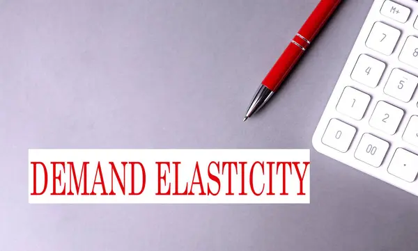 stock image DEMAND ELASTICITY text written on gray background with pen and calculator