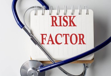 Arka planda tıbbi ekipman olan bir defterde RISK FACTOR sözcüğü