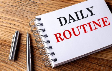 Ahşap zemin üzerinde kalem olan bir defter üzerindeki GÜN ROUTINE metni