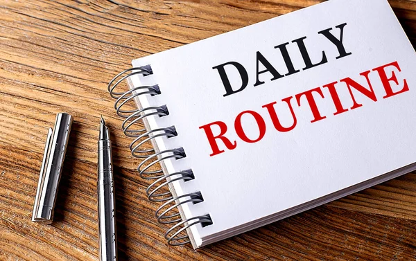 DAILY ROUTINE text on a notebook with pen on wooden background