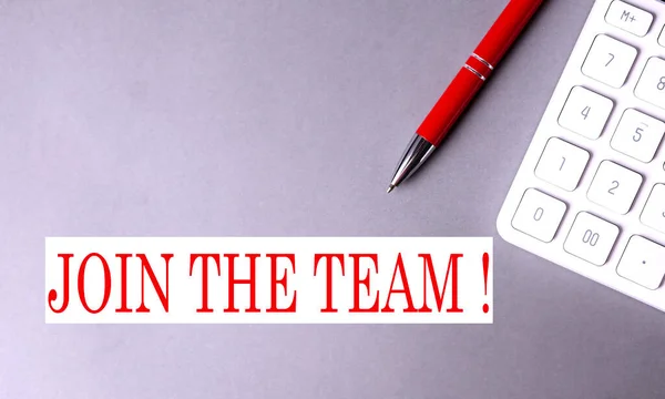 JOIN THE TEAM text written on gray background with pen and calculator