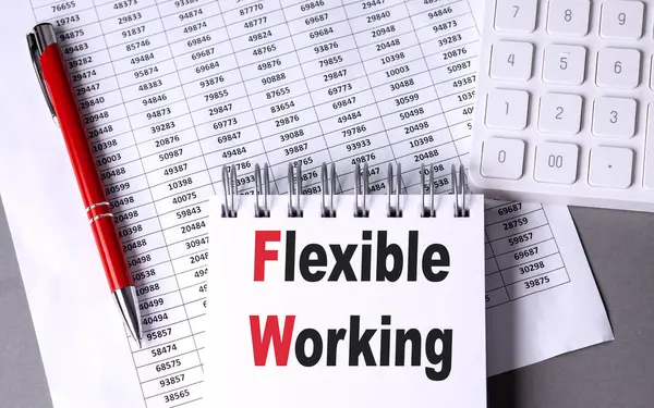 FLEXIBLE WORKING text on a notebook with pen, calculator and chart on grey background