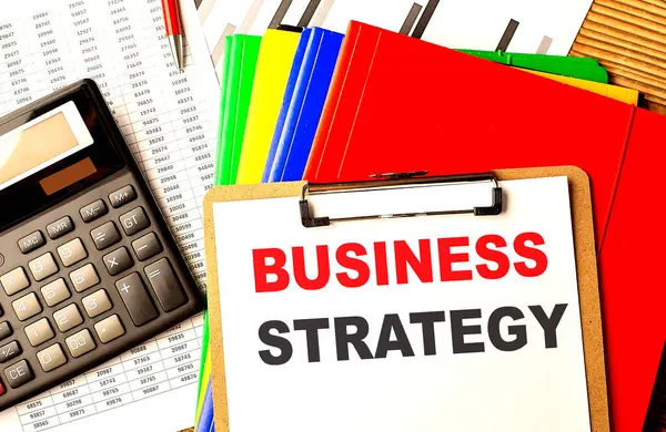 BUSINESS STRATEGY text written on a paper clipboard with chart and calculator