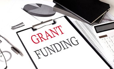 Arkaplanda çizelge ve defter olan bir kağıt pano üzerinde GRANT FUNDING metin