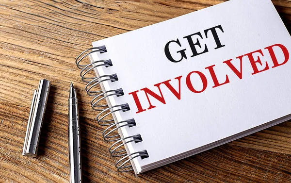GET INVOLVED text on a notebook with pen on wooden background