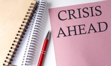CRISIS AHEAD kelime pembe kağıt üzerinde ofis araçları beyaz arka planda