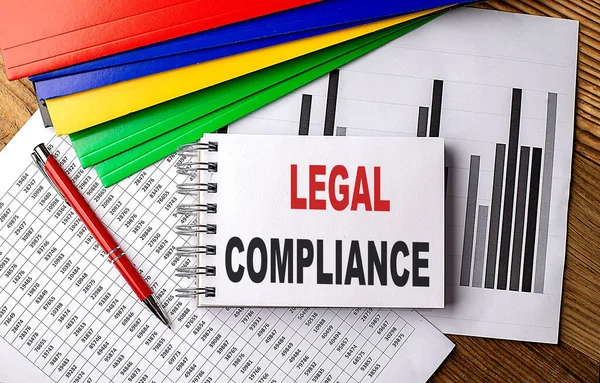LEGAL COMPLIANCE text on a notebook with pen, folder on a chart background