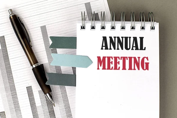 ANNUAL MEETING text on a notebook with pen, calculator and chart on a grey background