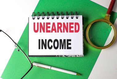 UNEARNED INCOME text on a notebook on green paper clipart