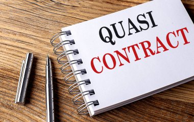 QUASI CONTRACT text on a notebook with pen on wooden background
