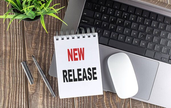 Ноутбук, мышь и ноутбук заметки с текстом НОВЫЙ РЕЛИЗ на деревянном фоне.