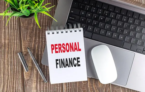 Diz üstü bilgisayar, fare ve defter notları ahşap bir arka planda PERSONAL finans.