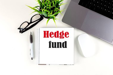 Dizüstü bilgisayarı, kalemi, gözlüğü ve faresi olan bir dizüstü bilgisayara yazılmış HEDGE FUND metni, beyaz arkaplan
