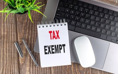 Tahta zemin üzerinde TAX EXEMPT metni bulunan dizüstü, fare ve defter notları.