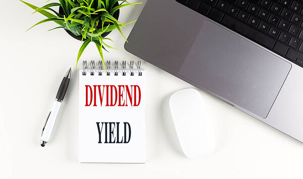 DIVIDEND YIELD text on a notebook with laptop, mouse and pen . 