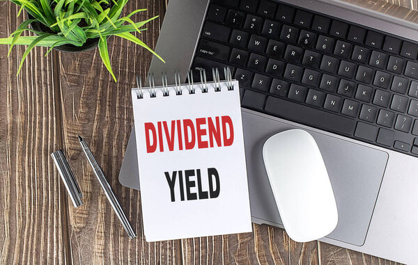 DIVIDEND YIELD text on a notebook with laptop, mouse and pen 