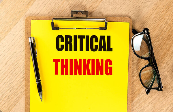 CRITICAL THINKING text on a yellow paper on clipboard with pen and glasses. 
