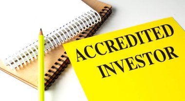 ACCREDITED INVESTOR text on a yellow paper with notebooks.  clipart