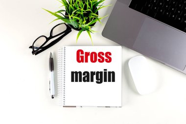 Dizüstü bilgisayarı, faresi ve kalemi olan bir defterde GROSS MARGIN metni . 