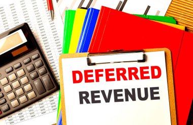 DEFERRED REVENUE text on a clipboard with calculator and color folder .  clipart