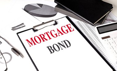 Not defteri ve hesap makinesiyle pano üzerinde mortGage BOND metni. 