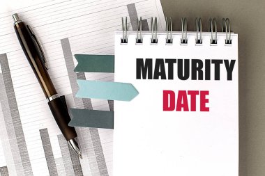 Gri arkaplan üzerinde çizelgesi olan bir defter üzerindeki MATURITY Tarih metni 