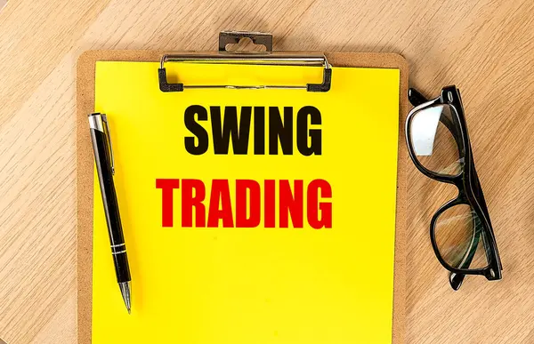 stock image SWING TRADING text on a yellow paper on clipboard with pen and glasses. 