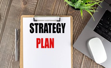 Diz üstü bilgisayarı, faresi ve kalemi olan bir pano kağıdındaki STRATEGY PLAN metni . 
