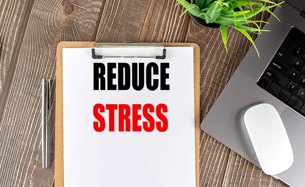 stock image REDUCE STRESS text on a clipboard paper with laptop, mouse and pen . 