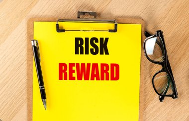 RISK REWARD text on yellow paper on a clipboard with pen and glasses.  clipart