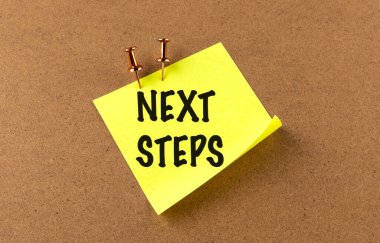 Bir tahta arkaplanındaki sarı yapışkan üzerine NEXT STEPS metni . 
