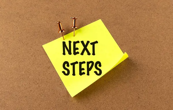Bir tahta arkaplanındaki sarı yapışkan üzerine NEXT STEPS metni . 