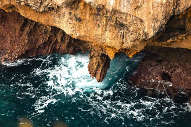 Dalgalar kayalık çıkıntının altındaki sivri kayalara çarpıyor, aşağıdaki köpüklü su . 
