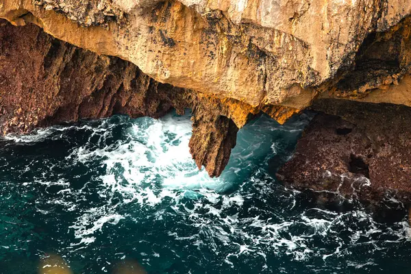 Dalgalar kayalık çıkıntının altındaki sivri kayalara çarpıyor, aşağıdaki köpüklü su . 
