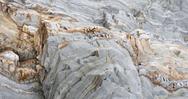Belirgin gri ve turuncu renkli katmanlı kaya oluşumu, karmaşık jeolojik dokular ve doğal desenler sergiliyor. . 