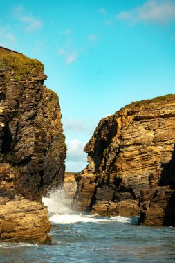 Dalgalar engebeli kıyı kayalıkları arasında çarpışıyor. Gökyüzü açık mavi. . 