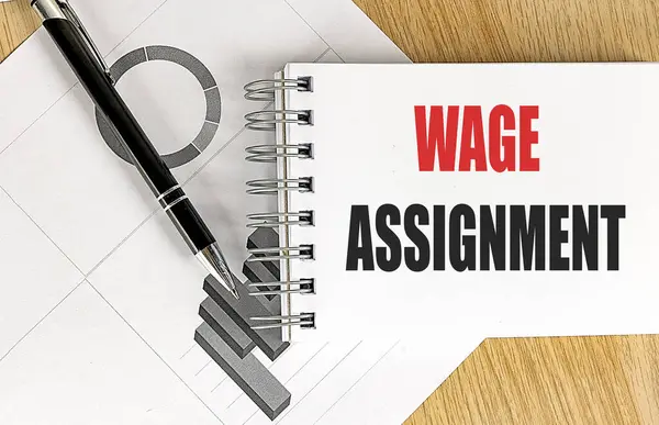 Stock image WAGE ASSIGNMENT text on notebook with chart on a wooden background 