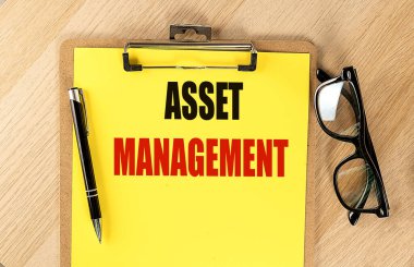 Kalem ve gözlüklü bir pano üzerinde sarı kağıt üzerinde ASSET MANAGEMENT metin. 
