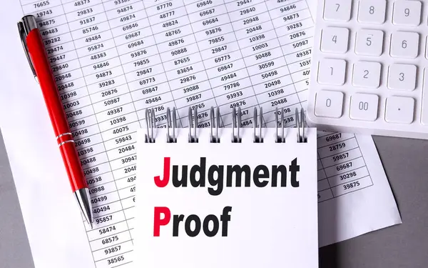 Çizelge, kalem ve hesap makineli bir defter üzerinde JUDGMENT PROOF metni. 